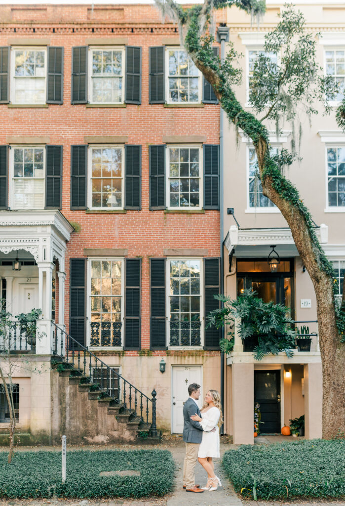 Engaged couple walking past a historic brick home on Jones Street in Savannah