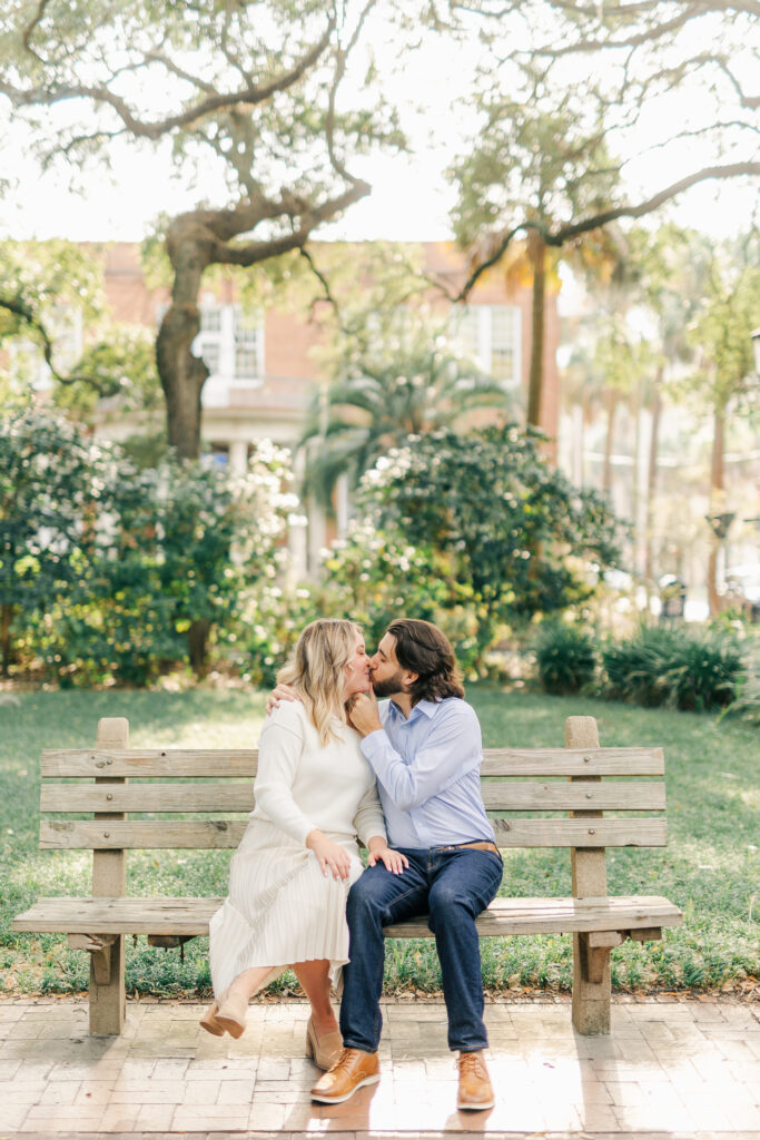 Engaged couple sitting together on a bench beneath the oak trees in Monterey Square