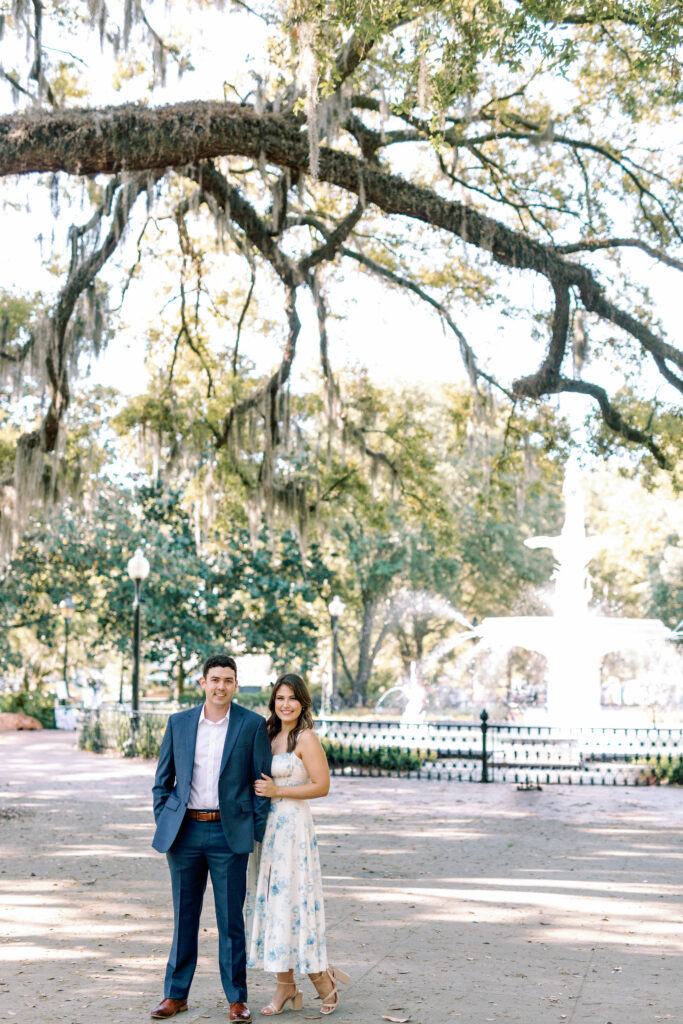 Engaged couple posing near the Forsyth Park fountain beneath Savannah oak trees