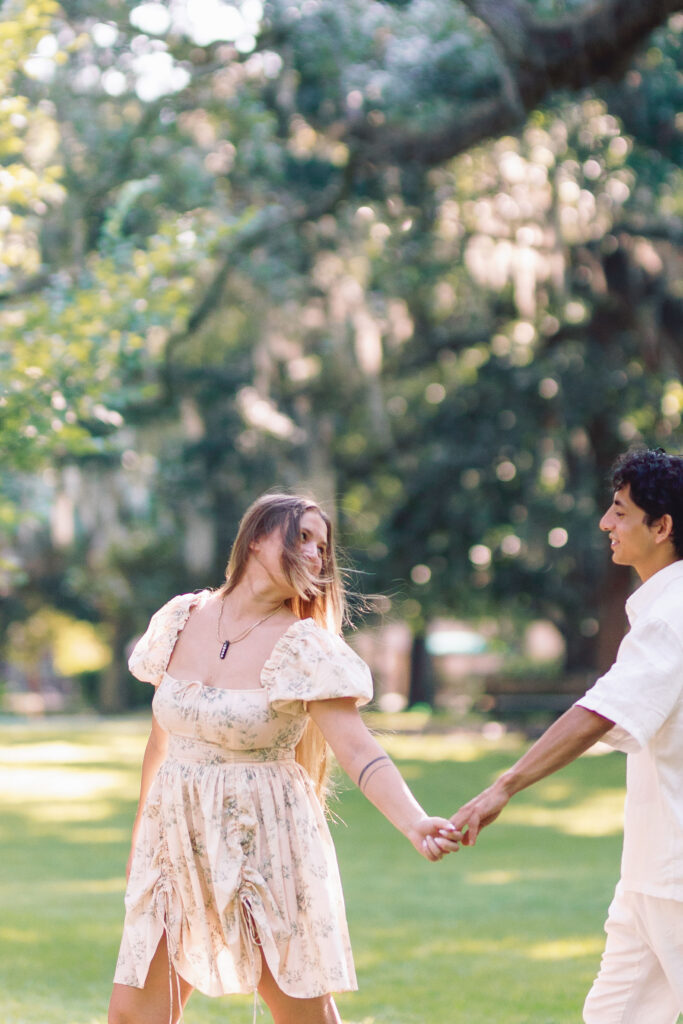 Couple holding hands and walking through the greenery at Forsyth Park in Savannah
