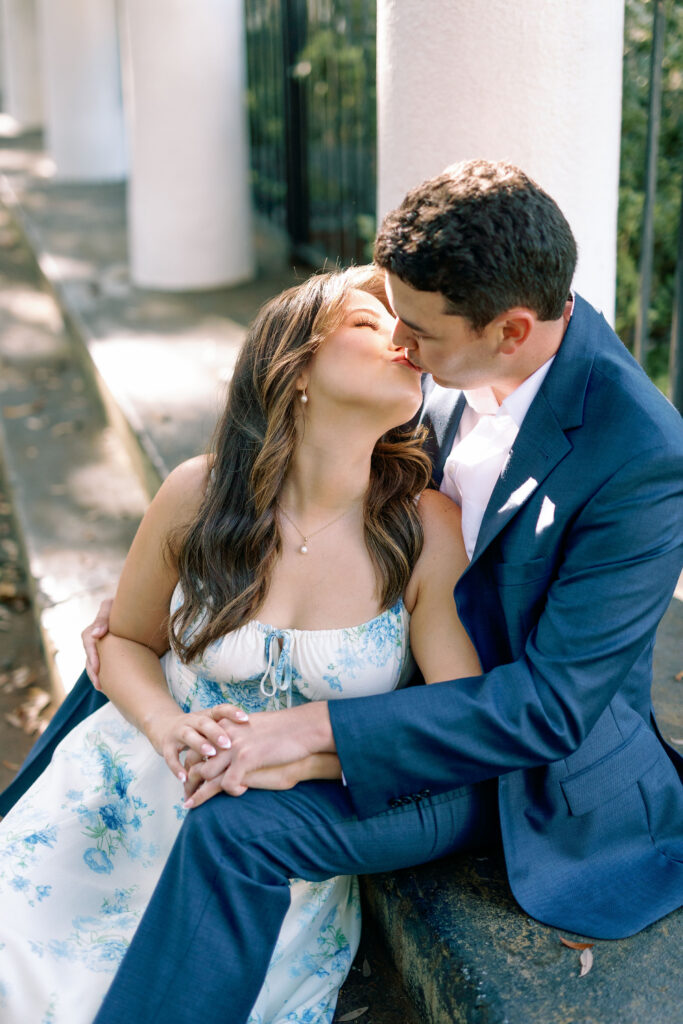 Close-up of an engaged couple kissing beside white columns near Forsyth Park