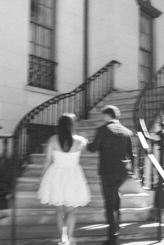 Black-and-white photo of an engaged couple running up the steps of a historic Savannah building